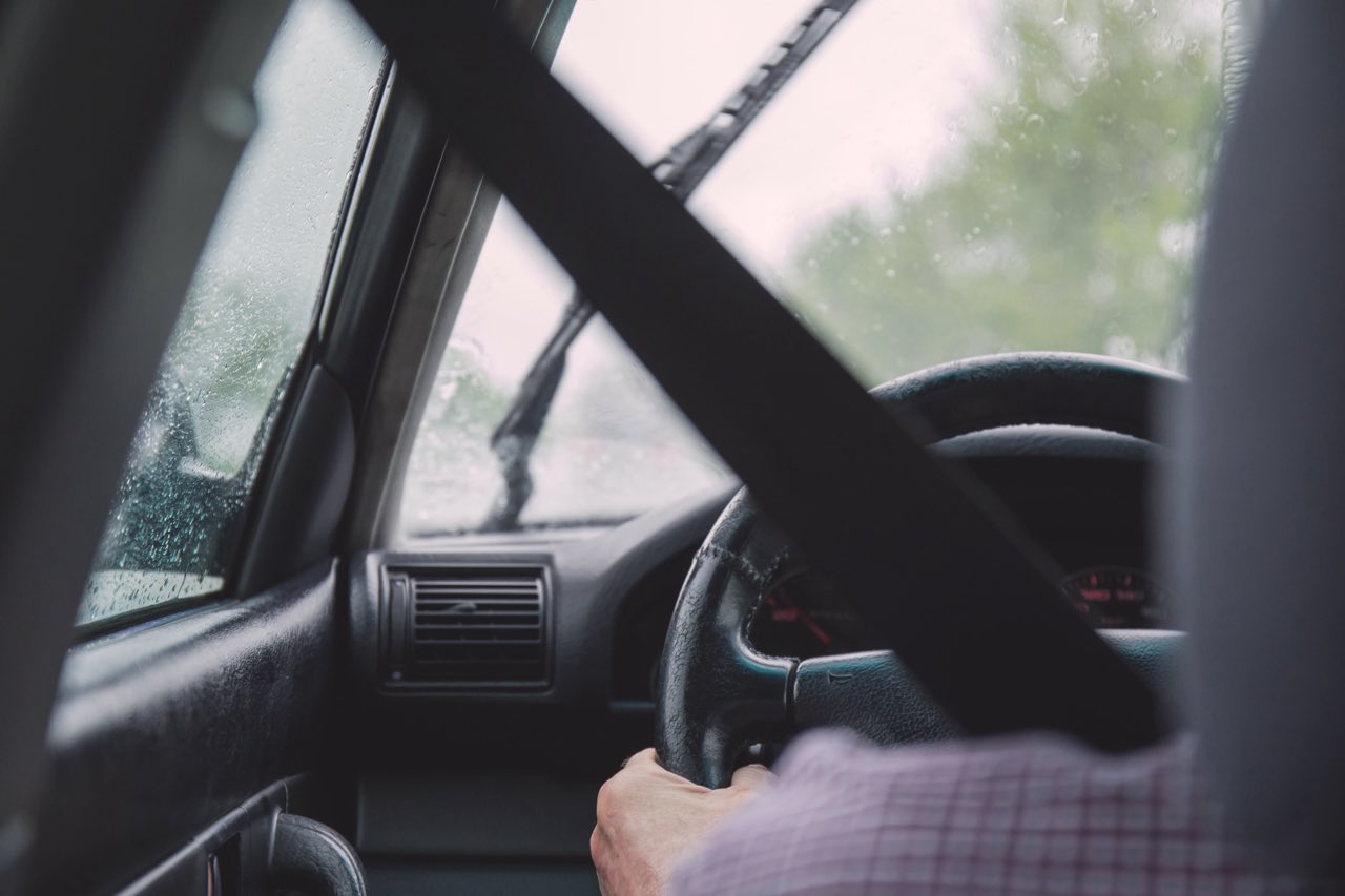 View from inside a vehicle cabin in wet weather, with the driver's three-point seat belt worn across the shoulder.