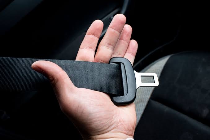 An open palm holding seat belt webbing and a black latch plate with its chrome tongue, presented flat for inspection.