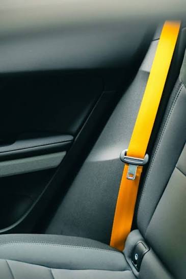 High-visibility orange seat belt webbing with a latch plate, running down the side of a dark vehicle interior.